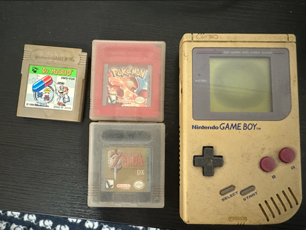 A yellowed Game Boy Classic with green-and-yellow screen, a cartridge of Pokémon Red, another of Zelda Link's Awakening DX, and another of Dr. Mario. They are all dirty and yellowed.